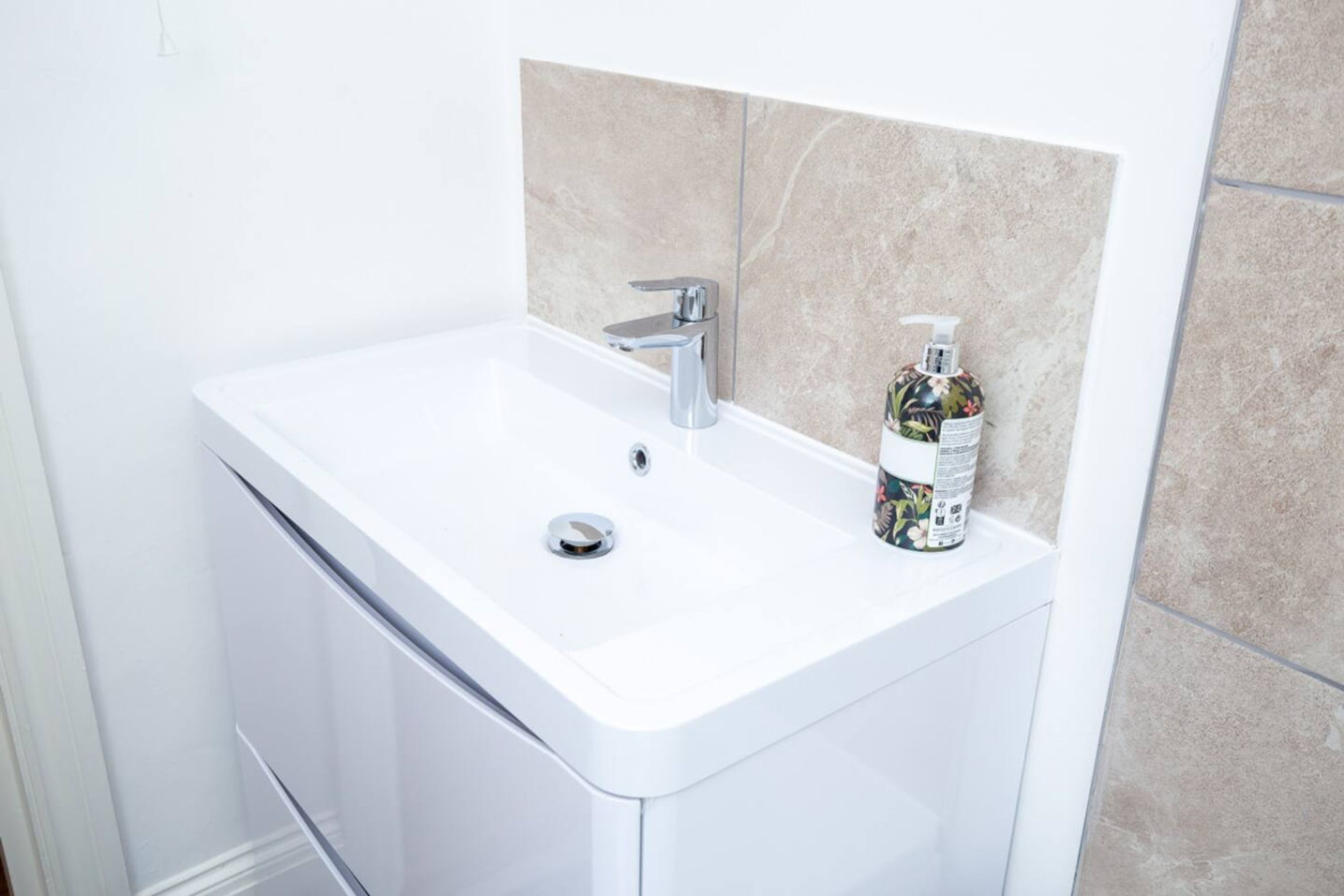 A white bathroom sink with a chrome faucet, a soap dispenser, and beige tiled walls.