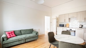 Ein modernes Wohnzimmer mit einem grünen Sofa, einem runden Tisch und einer Küche im Hintergrund.