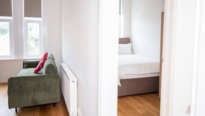 Ein Zimmer mit einem grünen Sofa, einem Bett mit weißer Bettwäsche und einem Fenster mit Jalousien.
