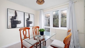 Un coin repas avec une table en verre, des chaises en bois et deux tableaux abstraits accrochés au mur.