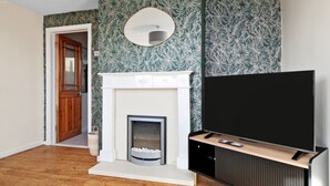 Un salon avec une cheminée, un téléviseur posé sur un meuble et une porte donnant sur une autre pièce.