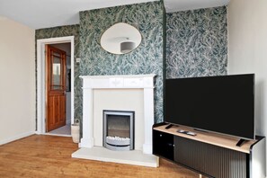 A living room with a fireplace, a television on a stand, and a door leading to another room. - Newly Renovated 3BR House Perfect for Families or Contractors (Plymouth)