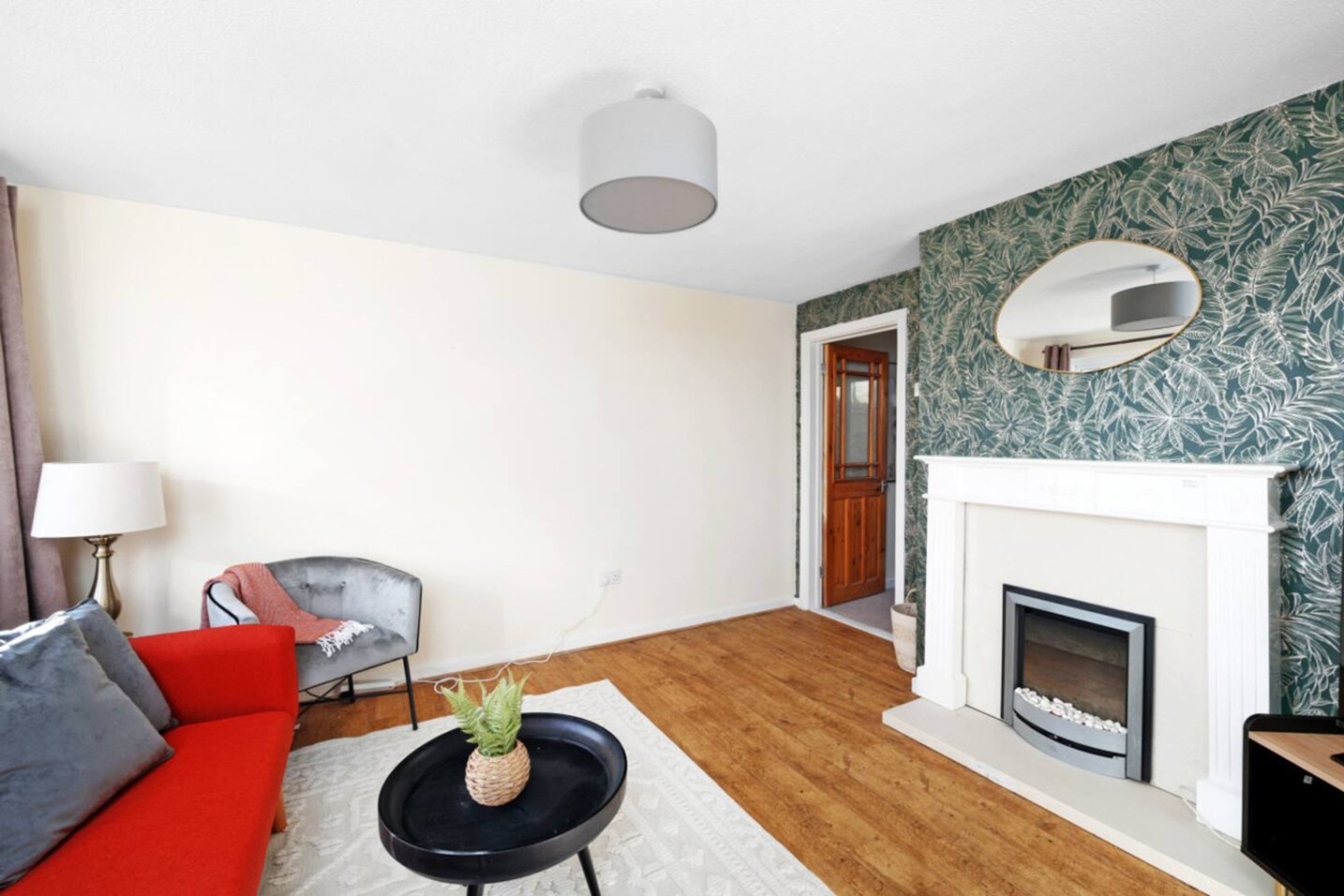 Ein Wohnzimmer mit einem roten Sofa, einem schwarzen Couchtisch mit einer Ananas, einem weißen Kamin und einem Spiegel an der Wand.