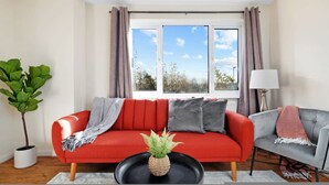 Un salon moderne avec un canapé rouge, un fauteuil gris, une table basse noire et une plante en pot.