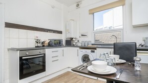 A modern kitchen with white cabinetry, a built-in oven, a microwave, and a washing machine. - Gloucester Street Nest - 3BR Flat for 7 Guests (Stroud)