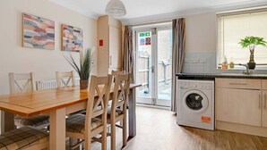 A kitchen with a washing machine, a dining area with a table and chairs, and a view through a door. - Harland Haven Spacious 4BR House in Ipswich (Ipswich)