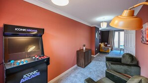 A room with a retro arcade machine, a sofa, and a lamp. - Harland Haven Spacious 4BR House in Ipswich (Ipswich)