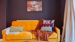 A room with a yellow sofa, a wall-mounted light, and a piece of abstract art. - Harland Haven Spacious 4BR House in Ipswich (Ipswich)