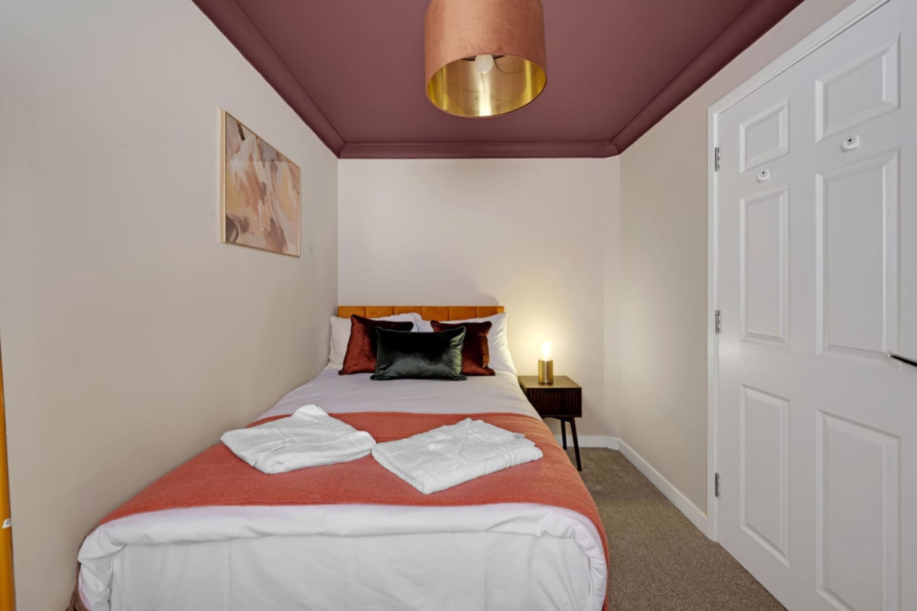 A hotel room with a bed, a bedside lamp, a painting on the wall, and a door.