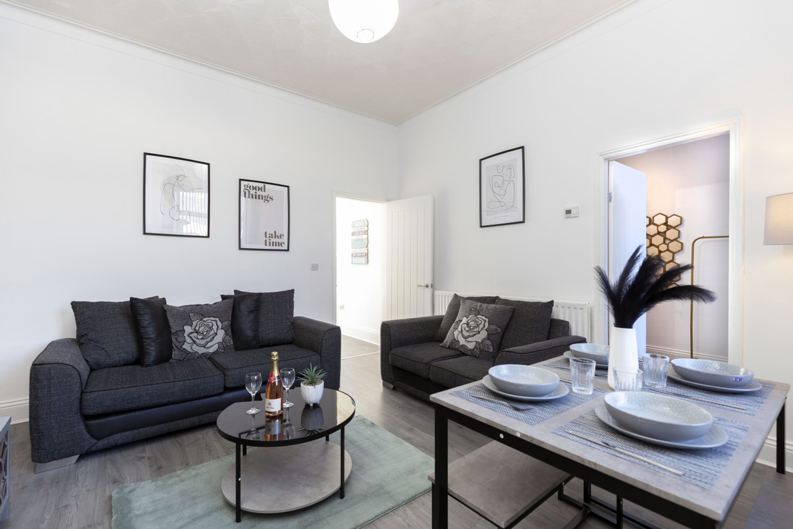 A modern living room with two grey sofas, a coffee table, and a dining table set with plates and glasses.
