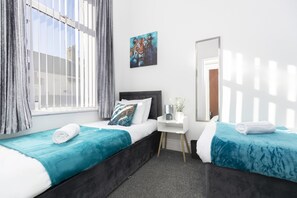 Ett hotellrum med två sängar, ett skrivbord, en stol, ett fönster med gardiner, en tavla på väggen och en spegel.