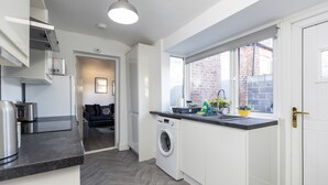 A modern kitchen with a washing machine, a countertop with appliances, and a window with a view of a brick building. - Newly Renovated 3BR House Near Hospital uni (Sunderland)