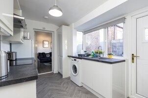 Una cocina moderna con lavadora, una encimera con electrodomésticos y una ventana que ofrece vistas a un edificio de ladrillo.