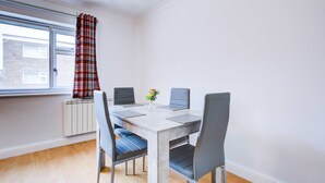 Ein Essbereich mit Tisch, Stühlen, einem Fenster mit Vorhängen und einer Heizung.