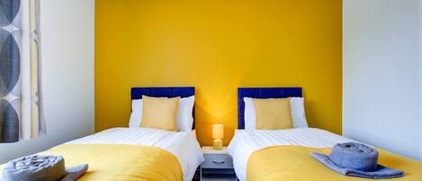 A hotel room with two beds, a nightstand, a lamp, and a towel on each bed.