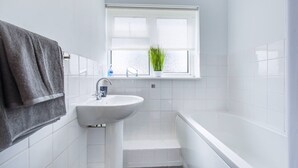 Ein Badezimmer mit Waschbecken, einem Fenster mit Pflanze, einem Handtuchhalter und einer Badewanne.