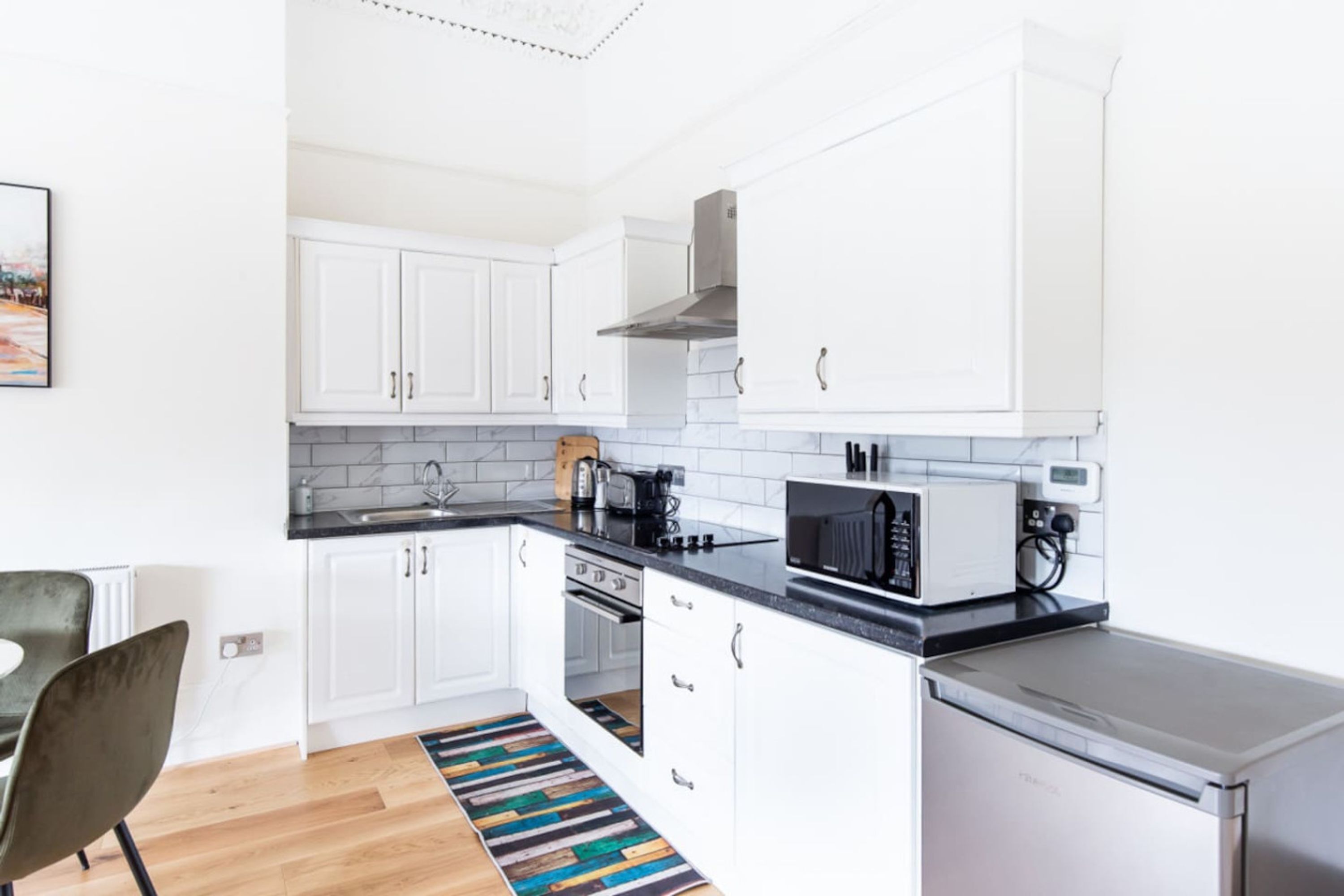 Una cocina compacta con armarios blancos, microondas, tostadora y refrigerador.