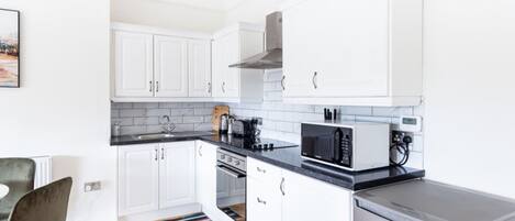Una cocina compacta con armarios blancos, microondas, tostadora y refrigerador.
