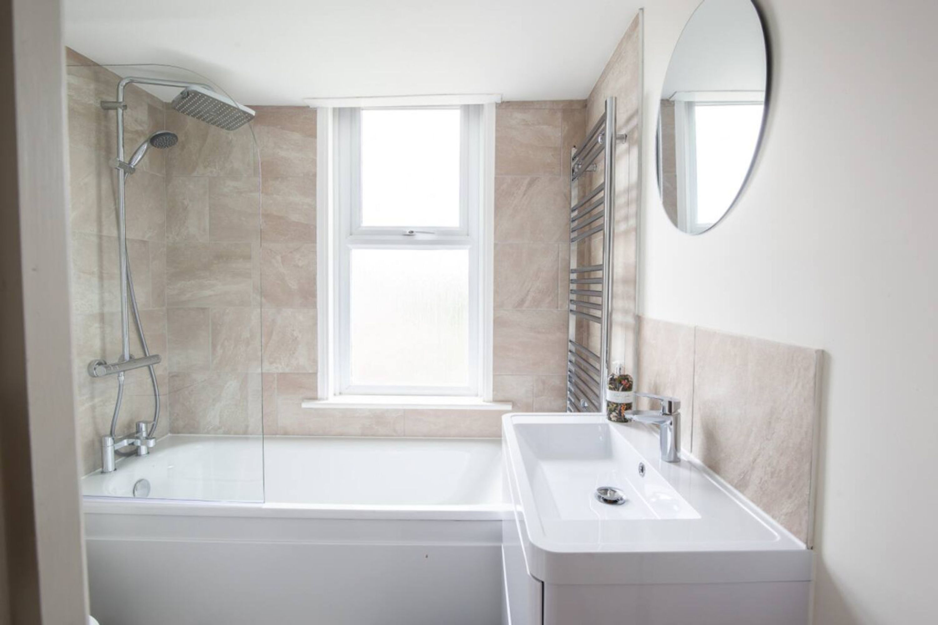 Een badkamer met een bad, een wastafel, een douche, een raam en een spiegel.