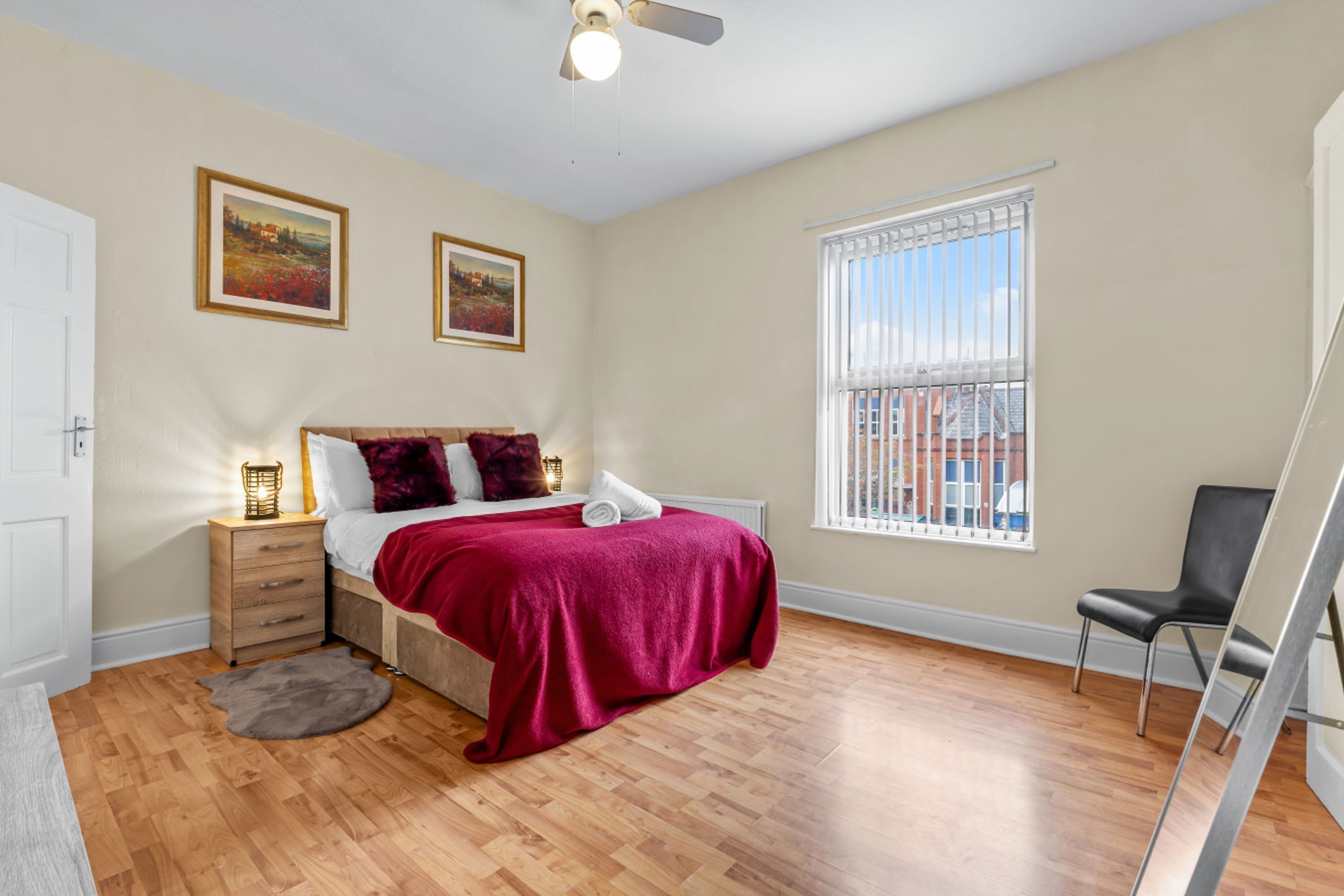 A bedroom with a bed, nightstand, chair, window, and artwork on the wall.