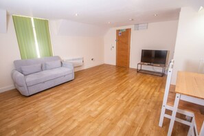 Ein Wohnzimmer mit grauem Sofa, Holzboden, einem Fernsehschrank und einer Tür.