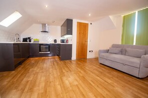 A modern kitchen with dark cabinets, a wooden floor, and a grey sofa in a living area. - Newly Renovated Sanctuary for 4 in Charlotte House (Ipswich)