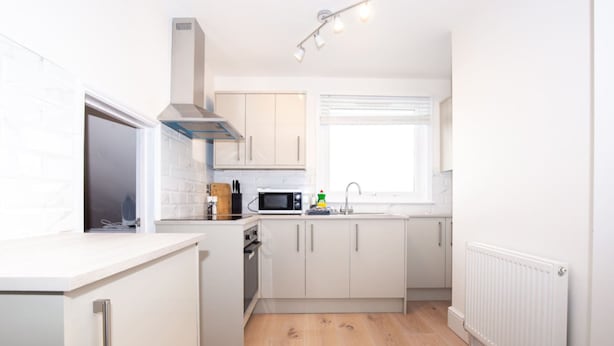 Una cocina moderna con armarios blancos, microondas, estufa y ventana con persianas.