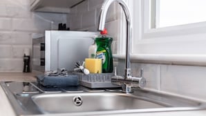 Un lavabo de cocina con un escurreplatos, una botella de detergente, una esponja y un grifo.