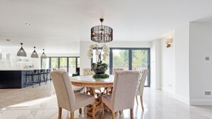 A modern kitchen with a round dining table, chairs, pendant lights, and a chandelier. - Mayrose House 6BR 4bath Luxe Spacious Retreat (Bishop's Stortford)