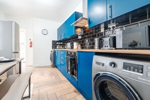 A modern kitchen with blue cabinets, a washing machine, and a microwave. - Newly Renovated 4BR House With Lots of Amenities (Bootle)