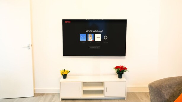 Ein Flachbildfernseher an der Wand, der eine Netflix-Oberfläche mit Profilsymbolen zeigt.