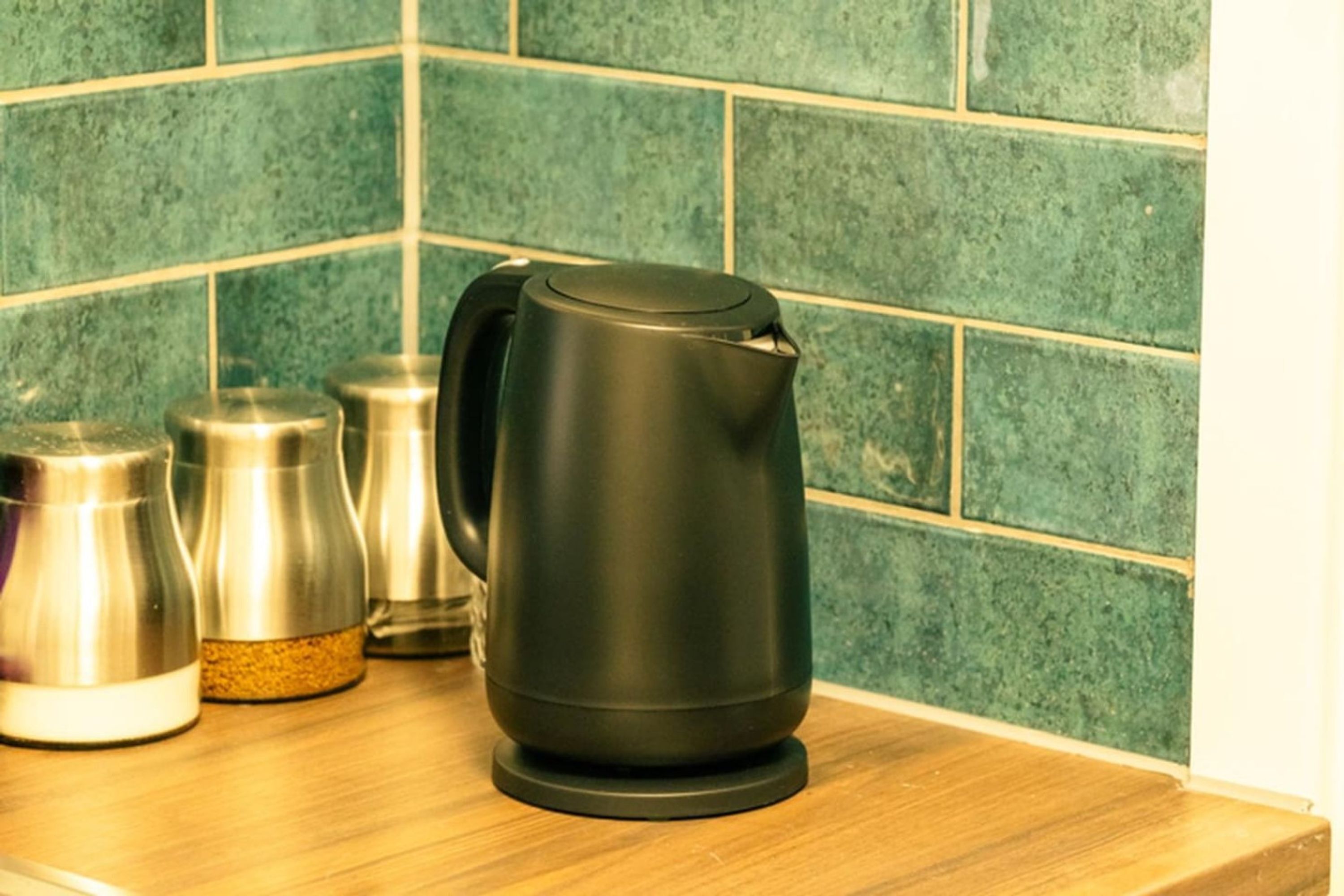 A kitchen counter with a black electric kettle, a stainless steel container, and a glass jar.
