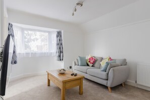 A living room with a sofa, a coffee table, and a window with curtains. - Charming 2-bedroom Escape in Worthing (Worthing)
