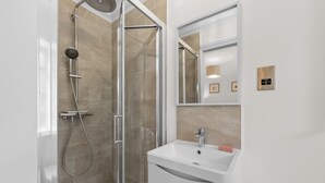 Ein modernes Badezimmer mit einer begehbaren Glasdusche, einem weißen Waschbecken und einem Spiegel darüber.