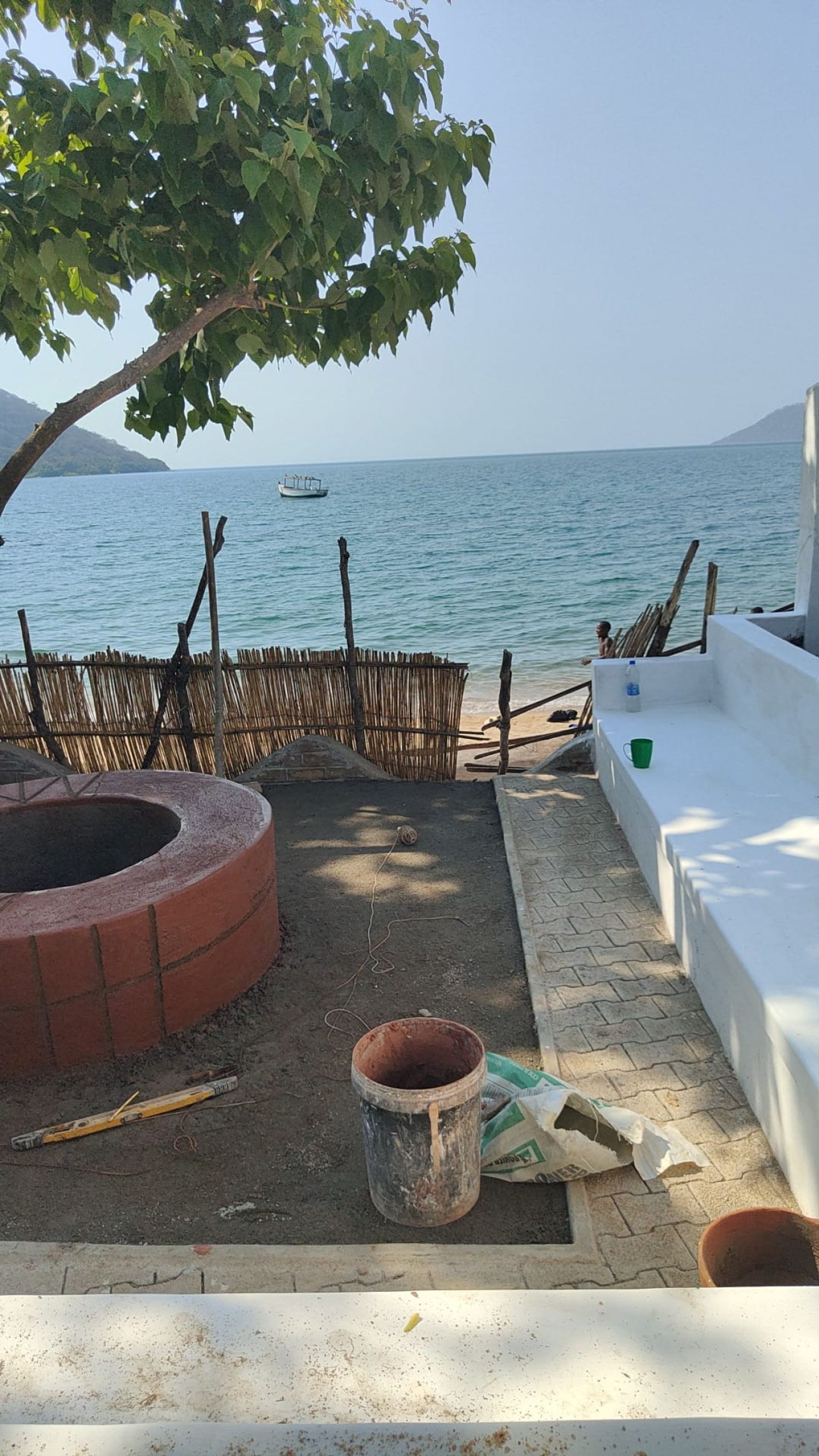 Un área de patio con un brasero de ladrillo, un cerco de madera y vista al mar.