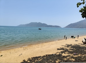 Una playa con agua tranquila, un bote y gente cerca de la orilla.