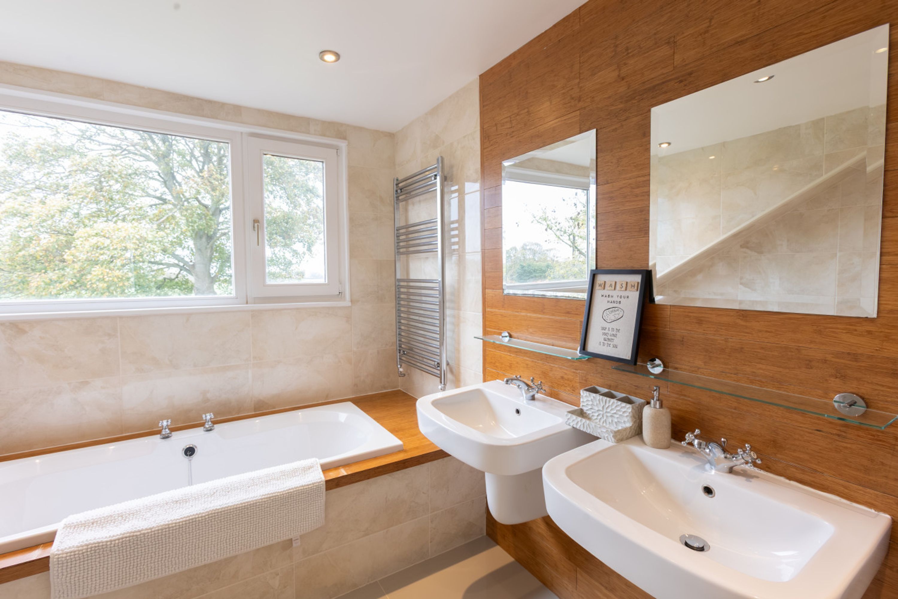 Ein modernes Badezimmer mit einer Badewanne, zwei Waschbecken, einem großen Spiegel und einem Fenster.
