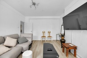 Een woonkamer met een bank, twee stoelen, een salontafel, een afstandsbediening en een plafondventilator.