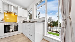 Una cocina moderna con armarios blancos, un salpicadero amarillo y vistas a un jardín verde a través de un ventanal amplio.