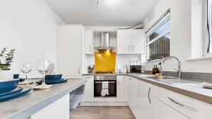 Una cocina moderna con armarios blancos, una campana extractora de acero inoxidable, horno empotrado y un ventanal grande.