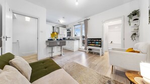 Una sala moderna con un sofá, una mesa de centro y un televisor. Cuenta con una cocina con una mesa de comedor y sillas.
