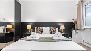 Una habitación de hotel moderna con una cama grande, dos mesitas de noche con lámparas, un cabecero floral y vistas del cielo a través de una ventana.