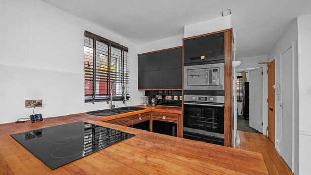 A modern kitchen with a black induction cooktop, wooden cabinets, a built-in oven, and a window with blinds. - Cozy 1-bed Flat in Croydon Sleeps 4 - Free Parking (Croydon)