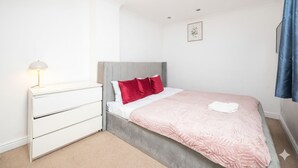 A bedroom with a bed, a bedside table, a lamp, and a wall-mounted picture. - Family-friendly 3-bed Haven in Northolt w Parking (Northolt)