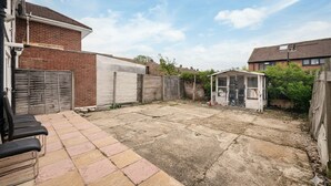 A backyard with a tiled patio, a shed, and a brick wall. - Family-friendly 3-bed Haven in Northolt w Parking (Northolt)