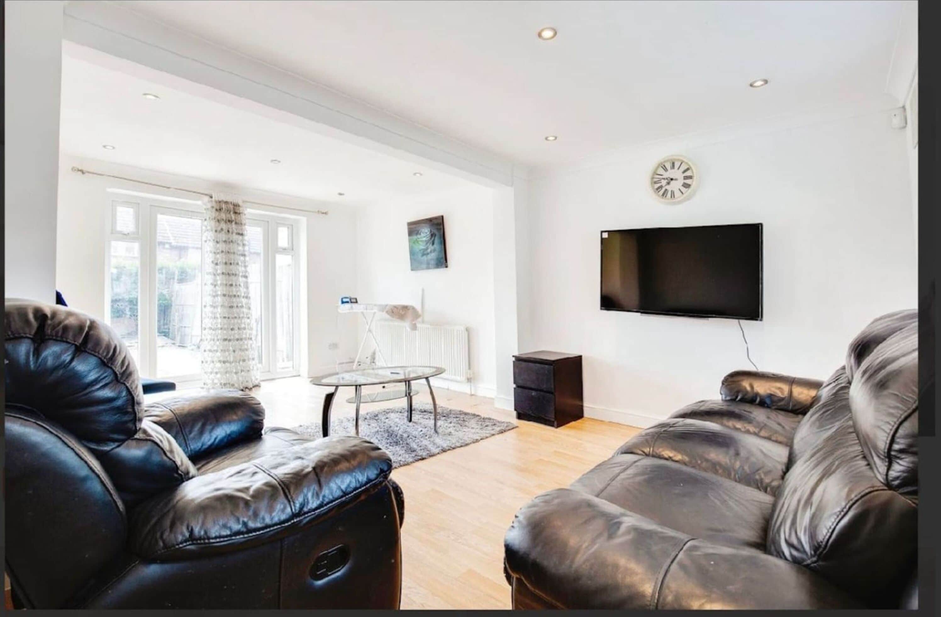 A living room with leather sofas, a glass coffee table, a flat-screen TV, and a clock on the wall.