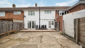 A residential property with a paved backyard, a wooden fence, and a garage door. - Family-friendly 3-bed Haven in Northolt w Parking (Northolt)
