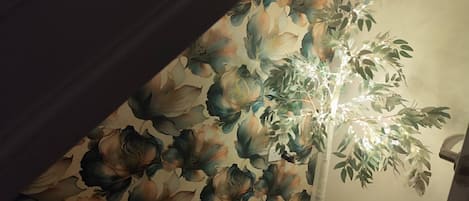 Una habitación con papel tapiz floral, una lámpara de pie blanca y una puerta.