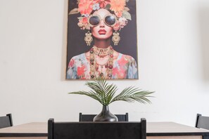 A dining area with a table, chairs, a vase with a plant, and a large floral painting on the wall. - The Ipswich Snug Spacious 3BR Retreat Free Parking (Ipswich)