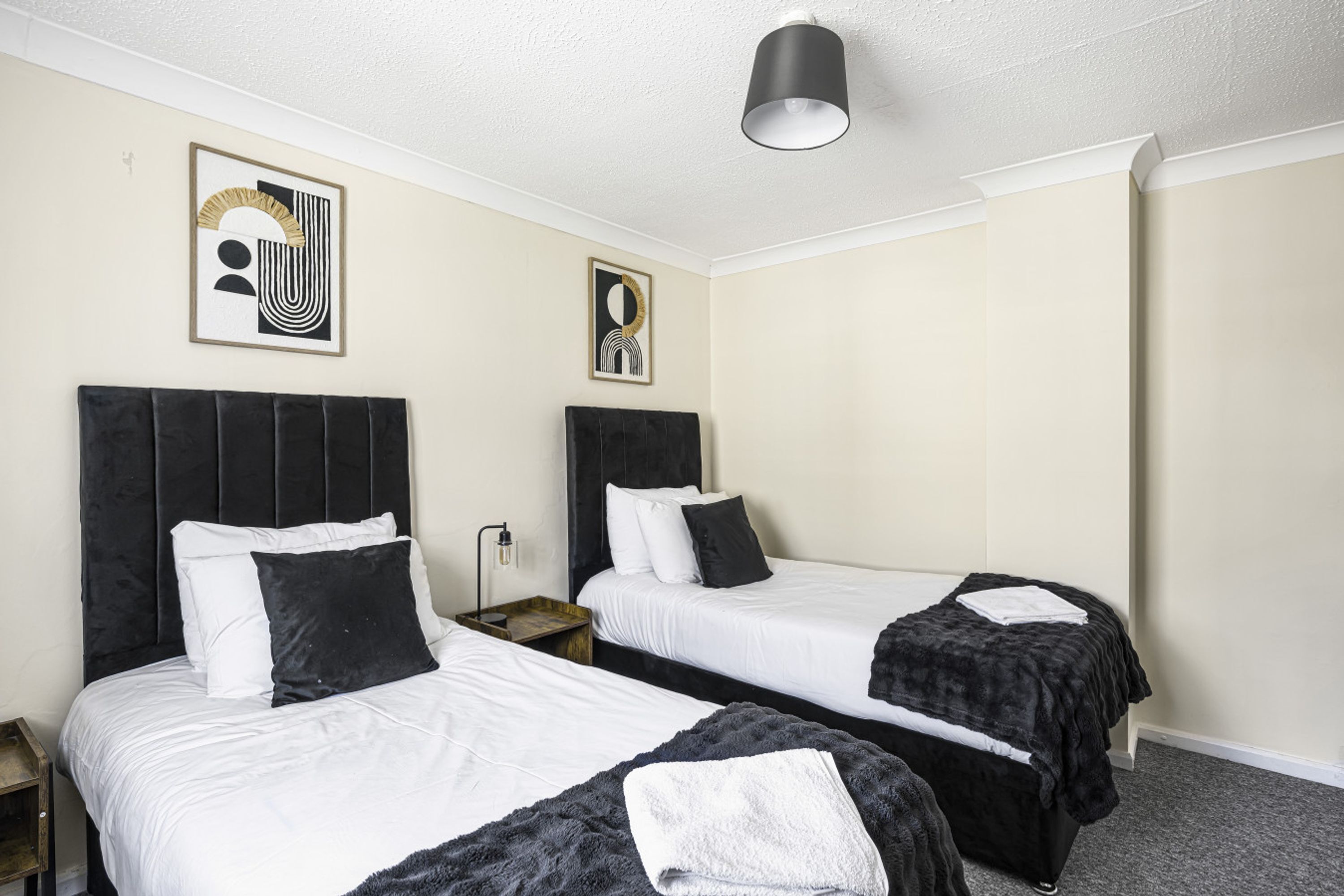 Habitación de hotel con dos camas, una lámpara de techo y dos cuadros enmarcados en la pared.